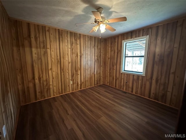 unfurnished room with wooden walls, dark hardwood / wood-style flooring, ceiling fan, and a textured ceiling