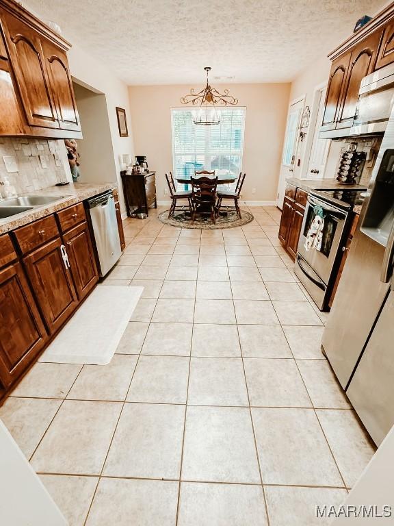 kitchen with decorative light fixtures, a textured ceiling, a notable chandelier, light tile patterned flooring, and stainless steel appliances