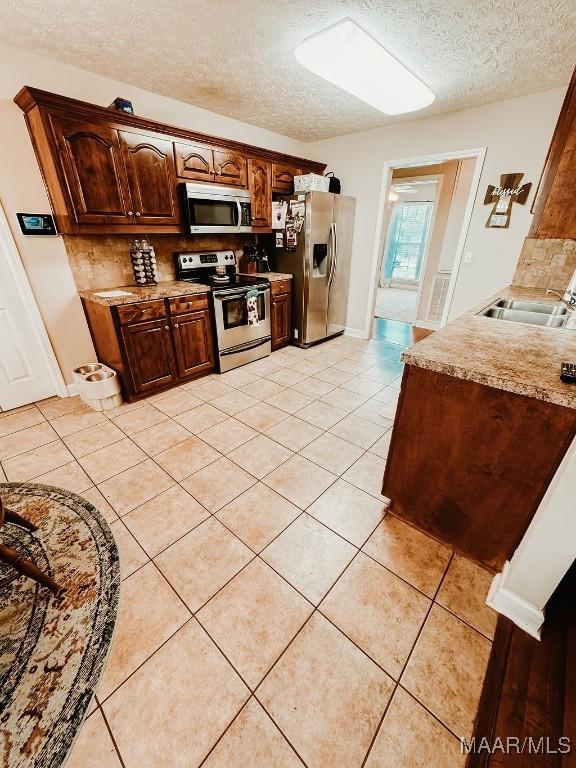 kitchen featuring sink, light tile patterned flooring, a textured ceiling, and appliances with stainless steel finishes