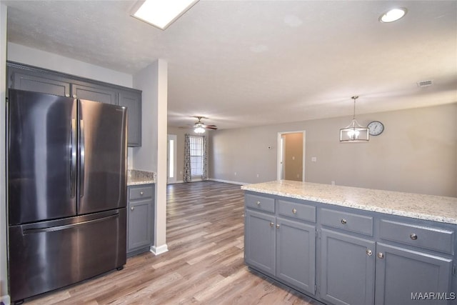 kitchen with light stone countertops, ceiling fan, stainless steel fridge, pendant lighting, and light hardwood / wood-style flooring