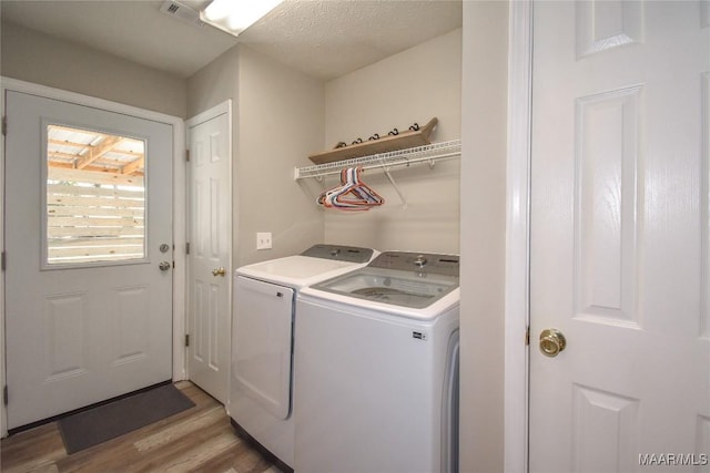 clothes washing area featuring separate washer and dryer, light hardwood / wood-style floors, and a textured ceiling