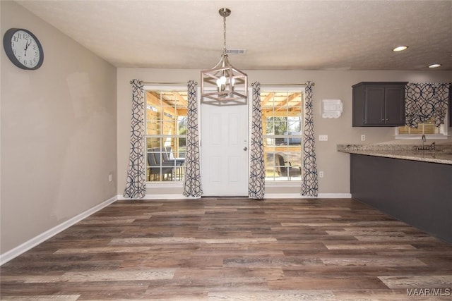 unfurnished dining area with sink, a textured ceiling, a notable chandelier, and dark hardwood / wood-style floors