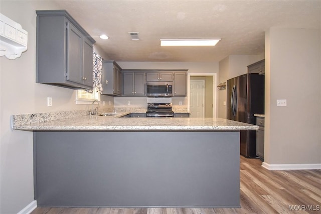 kitchen featuring kitchen peninsula, hardwood / wood-style flooring, stainless steel appliances, gray cabinets, and sink