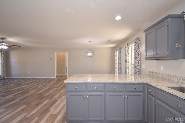 kitchen with light stone counters, ceiling fan, hardwood / wood-style flooring, kitchen peninsula, and gray cabinetry