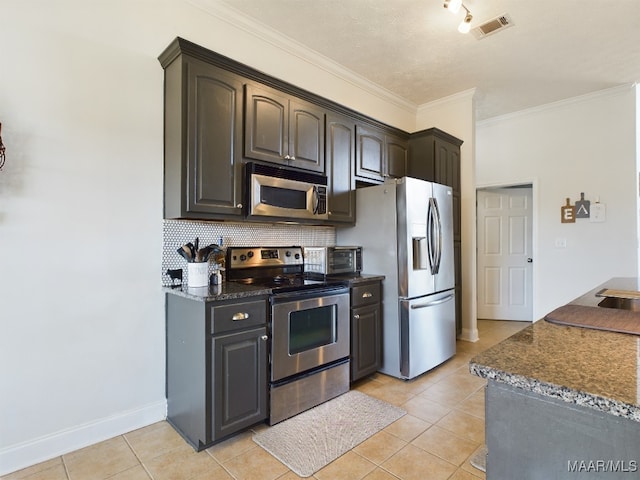 kitchen with dark stone countertops, light tile patterned floors, ornamental molding, and appliances with stainless steel finishes