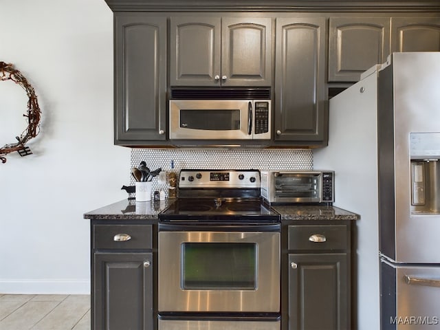 kitchen featuring appliances with stainless steel finishes, tasteful backsplash, light tile patterned floors, and dark stone counters