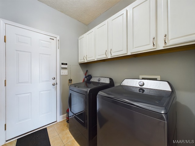 laundry room with light tile patterned flooring, cabinets, a textured ceiling, and washing machine and clothes dryer