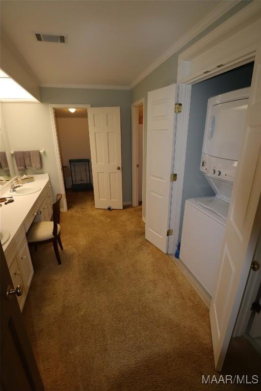 interior space featuring stacked washing maching and dryer, vanity, crown molding, and visible vents