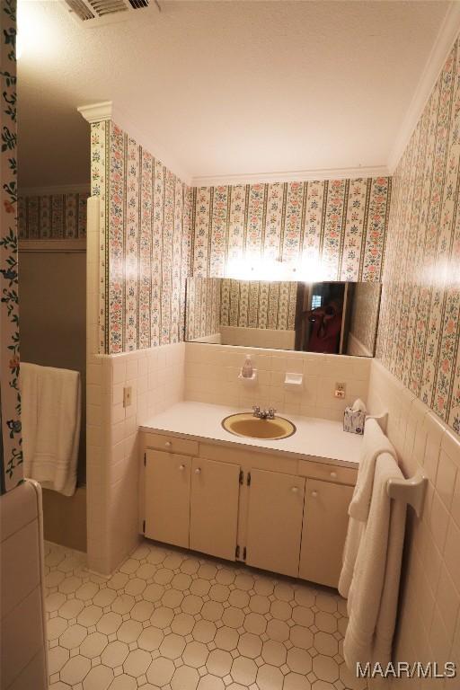 bathroom with visible vents, vanity, wainscoting, tile walls, and wallpapered walls
