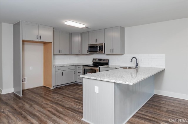 kitchen featuring sink, light stone counters, dark hardwood / wood-style flooring, kitchen peninsula, and appliances with stainless steel finishes