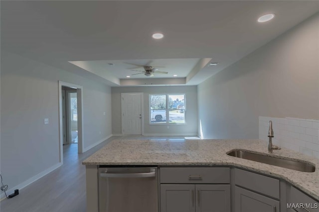 kitchen with light stone countertops, a tray ceiling, stainless steel dishwasher, a sink, and recessed lighting