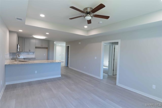 kitchen featuring visible vents, backsplash, gray cabinetry, a sink, and baseboards