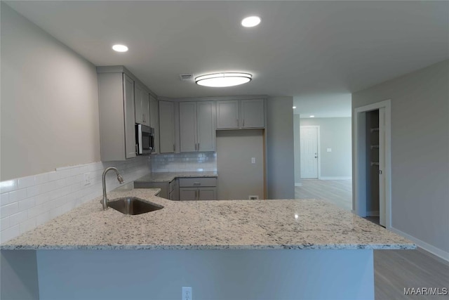 kitchen featuring light stone countertops, stainless steel microwave, a sink, and gray cabinetry