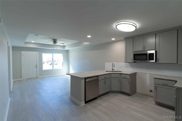 kitchen with appliances with stainless steel finishes, a tray ceiling, gray cabinets, and a sink