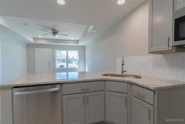 kitchen featuring a raised ceiling, appliances with stainless steel finishes, a sink, light stone countertops, and backsplash