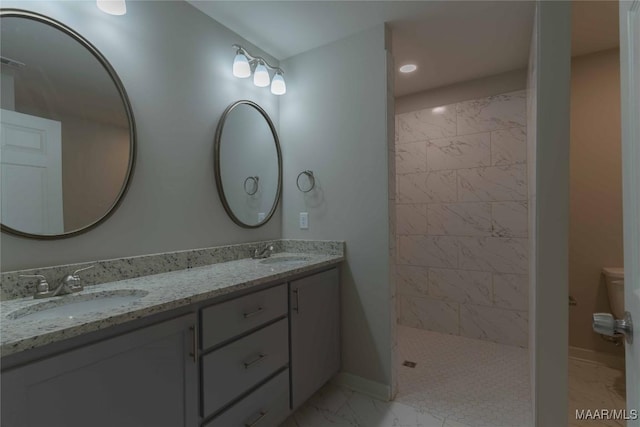 bathroom featuring marble finish floor, double vanity, tiled shower, and a sink