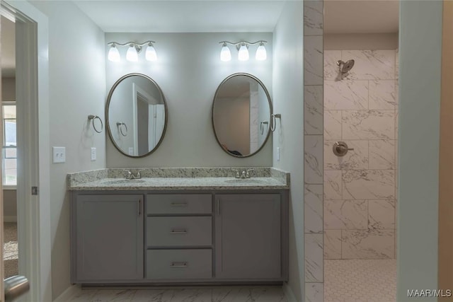 bathroom featuring marble finish floor, a sink, a tile shower, and double vanity