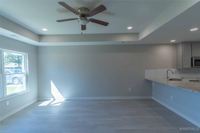 kitchen with light stone counters, stainless steel microwave, a sink, and baseboards