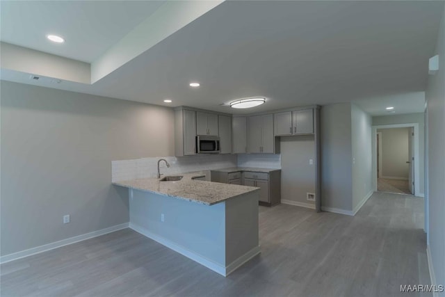 kitchen featuring light stone counters, a peninsula, a sink, gray cabinets, and stainless steel microwave