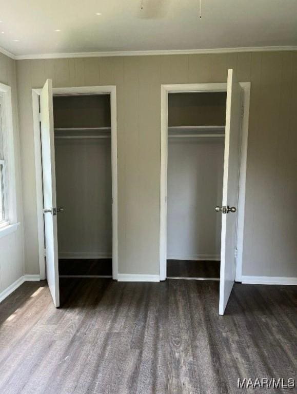 unfurnished bedroom with ornamental molding, dark hardwood / wood-style flooring, and multiple closets