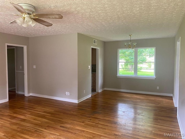 empty room with ceiling fan with notable chandelier, dark hardwood / wood-style floors, and a textured ceiling