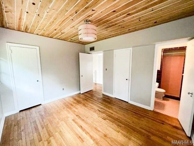 unfurnished bedroom featuring hardwood / wood-style flooring, ensuite bath, and wood ceiling