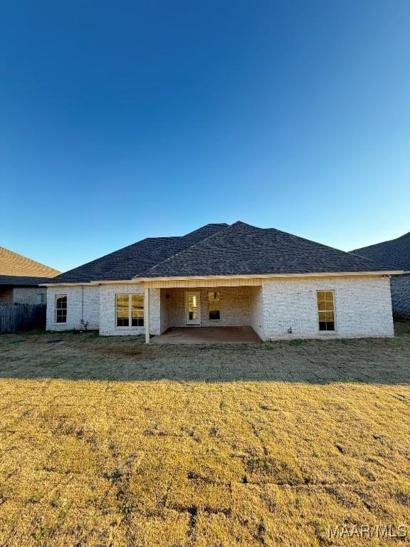 back of property featuring a patio area, a shingled roof, and a lawn