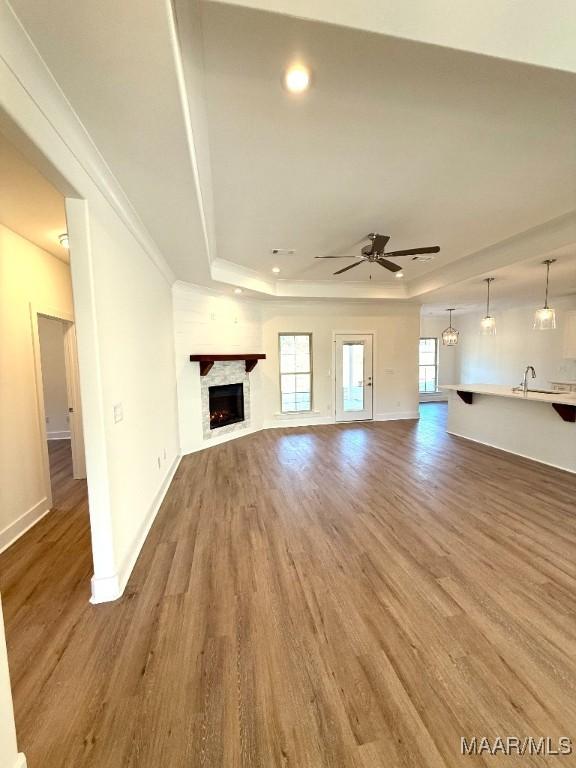 unfurnished living room featuring a tray ceiling, a fireplace, baseboards, and wood finished floors