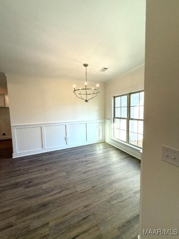 unfurnished dining area featuring dark wood-type flooring, wainscoting, visible vents, and a notable chandelier