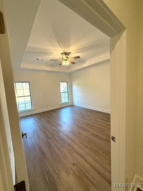 spare room with ceiling fan, baseboards, a raised ceiling, and dark wood-style flooring