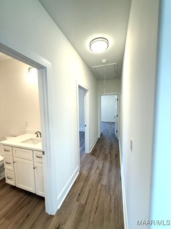 hallway featuring attic access, baseboards, dark wood-style flooring, and a sink