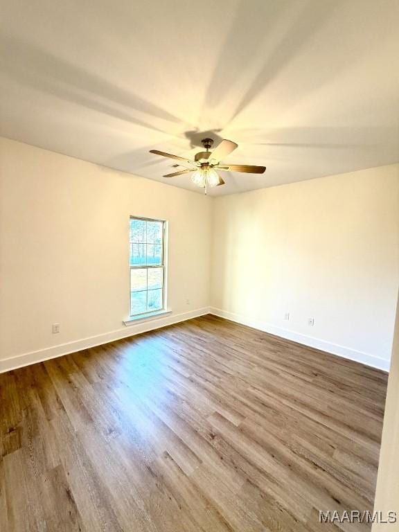 spare room featuring dark wood-style flooring, ceiling fan, and baseboards