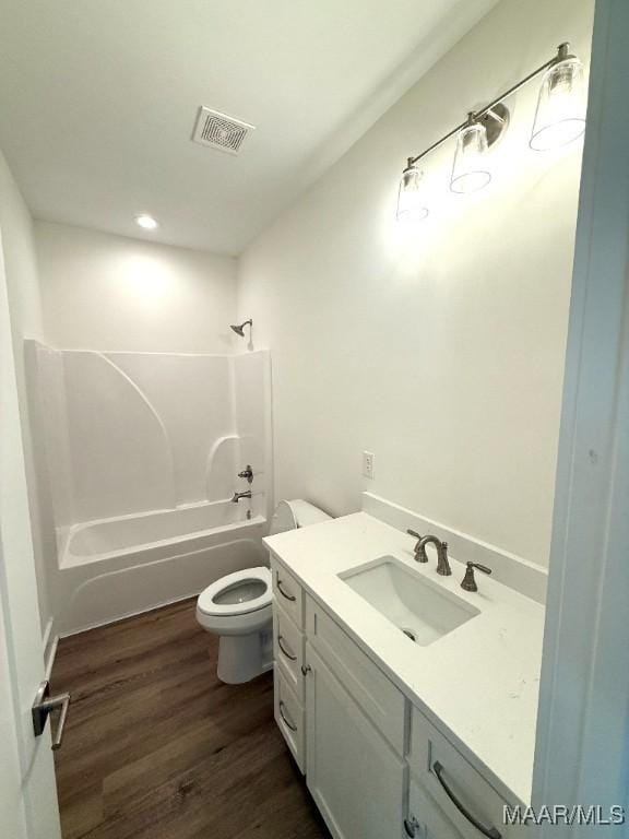 bathroom featuring toilet, wood finished floors, vanity, visible vents, and shower / washtub combination