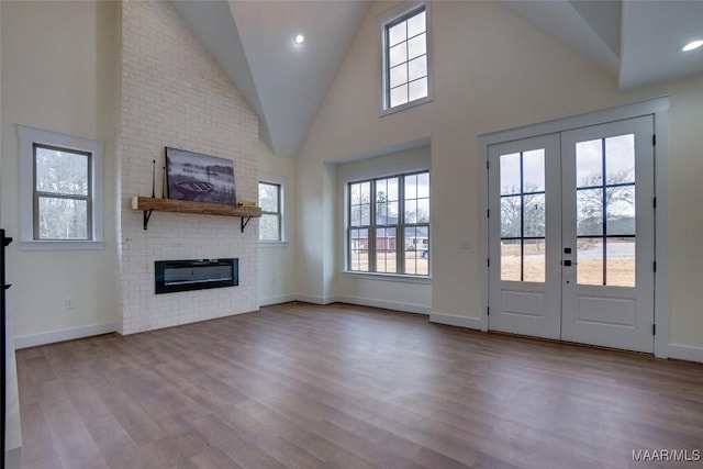 unfurnished living room featuring a brick fireplace, light wood-type flooring, high vaulted ceiling, and french doors