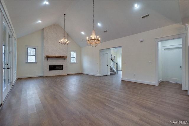 unfurnished living room featuring a fireplace, high vaulted ceiling, a notable chandelier, and hardwood / wood-style flooring