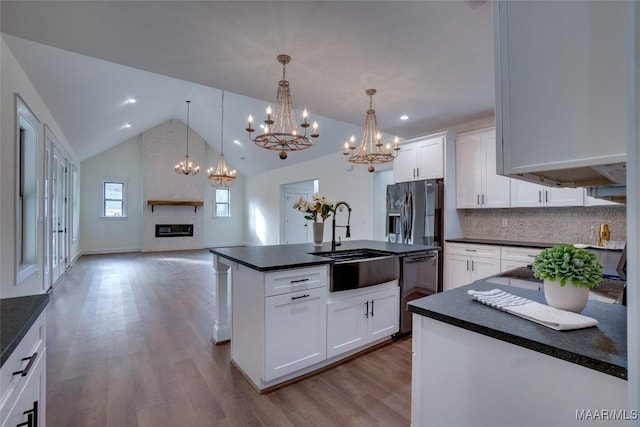 kitchen with a brick fireplace, sink, decorative light fixtures, white cabinets, and an island with sink