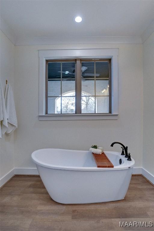 bathroom with ornamental molding, hardwood / wood-style flooring, and a bathing tub