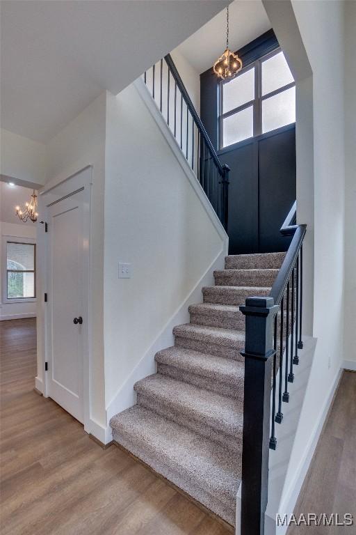 staircase with hardwood / wood-style floors and an inviting chandelier