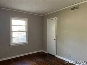 empty room featuring a wealth of natural light, crown molding, and dark wood-type flooring