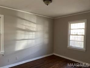 empty room with dark hardwood / wood-style floors, crown molding, and a healthy amount of sunlight