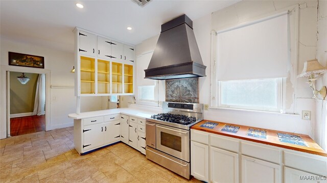 kitchen featuring premium range hood, stainless steel gas range oven, and white cabinetry