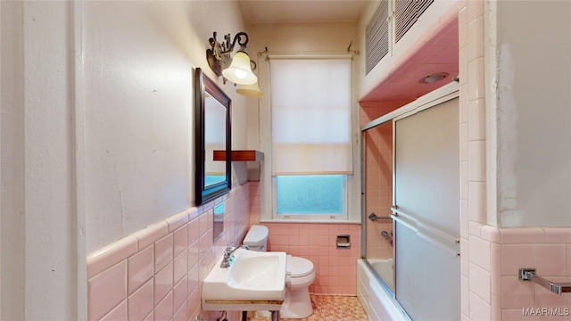 full bathroom with shower / bath combination with glass door, sink, tile walls, and toilet