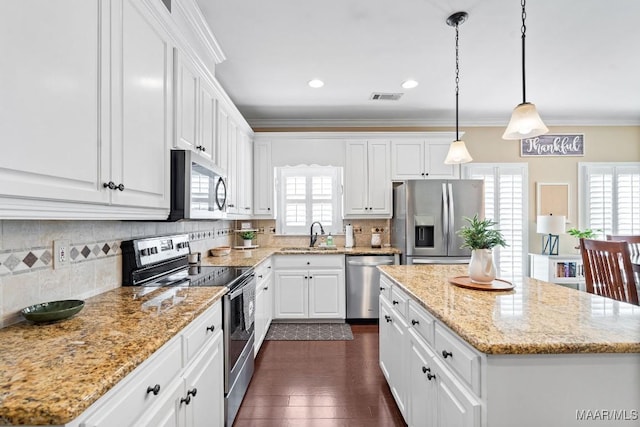 kitchen featuring a center island, hanging light fixtures, decorative backsplash, white cabinets, and appliances with stainless steel finishes