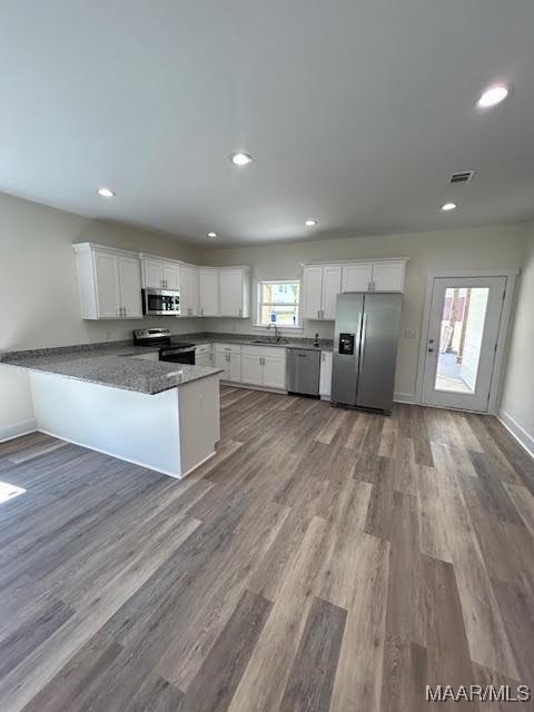 kitchen with kitchen peninsula, stainless steel appliances, sink, wood-type flooring, and white cabinets