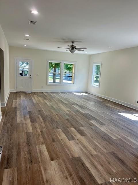 unfurnished living room featuring ceiling fan, a healthy amount of sunlight, and dark hardwood / wood-style flooring