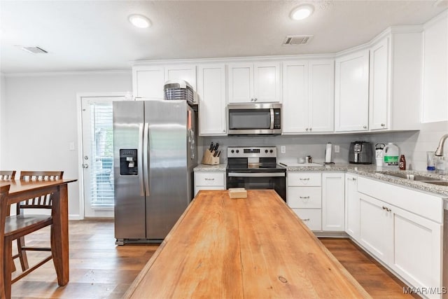 kitchen with appliances with stainless steel finishes, butcher block countertops, white cabinetry, and sink