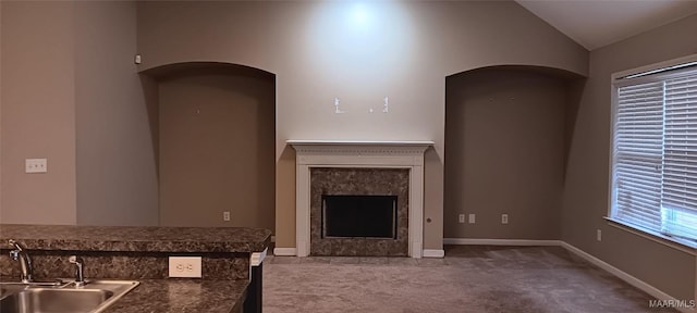 unfurnished living room with a tiled fireplace, sink, carpet floors, and lofted ceiling