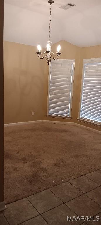 spare room featuring dark tile patterned flooring, an inviting chandelier, and vaulted ceiling