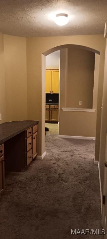 hall featuring dark carpet and a textured ceiling