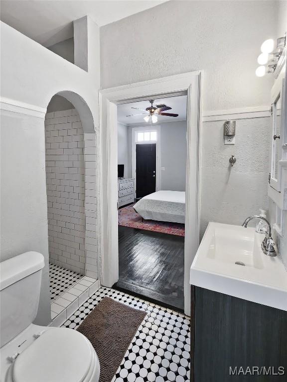 bathroom with vanity, ceiling fan, toilet, and tiled shower